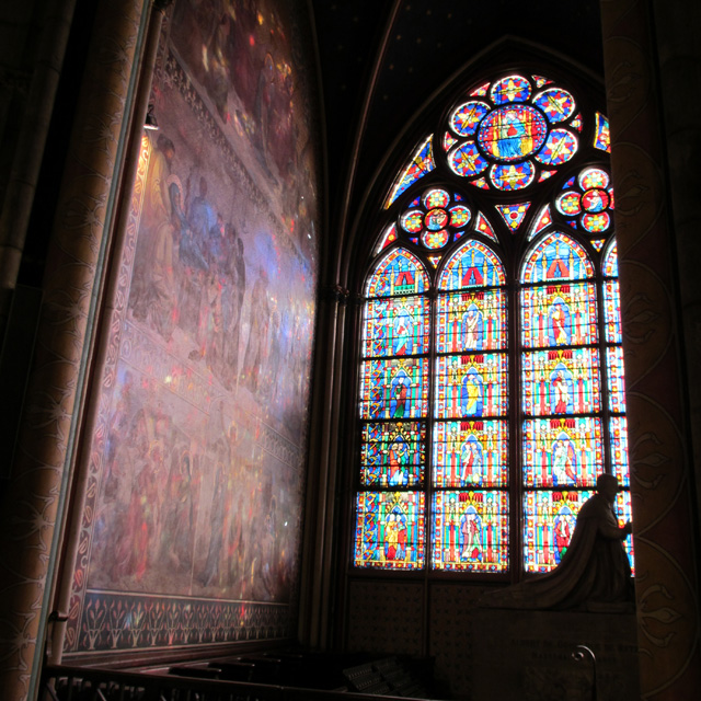 A statue in silhouette in front of a stained glass Notre-Dame window